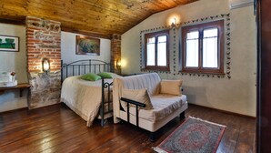 A cozy room with a wooden ceiling, a brick wall, a bed with a green pillow, a sofa, and two windows with decorative frames. - Agriturismo Borg da Ocjs (Cormons)
