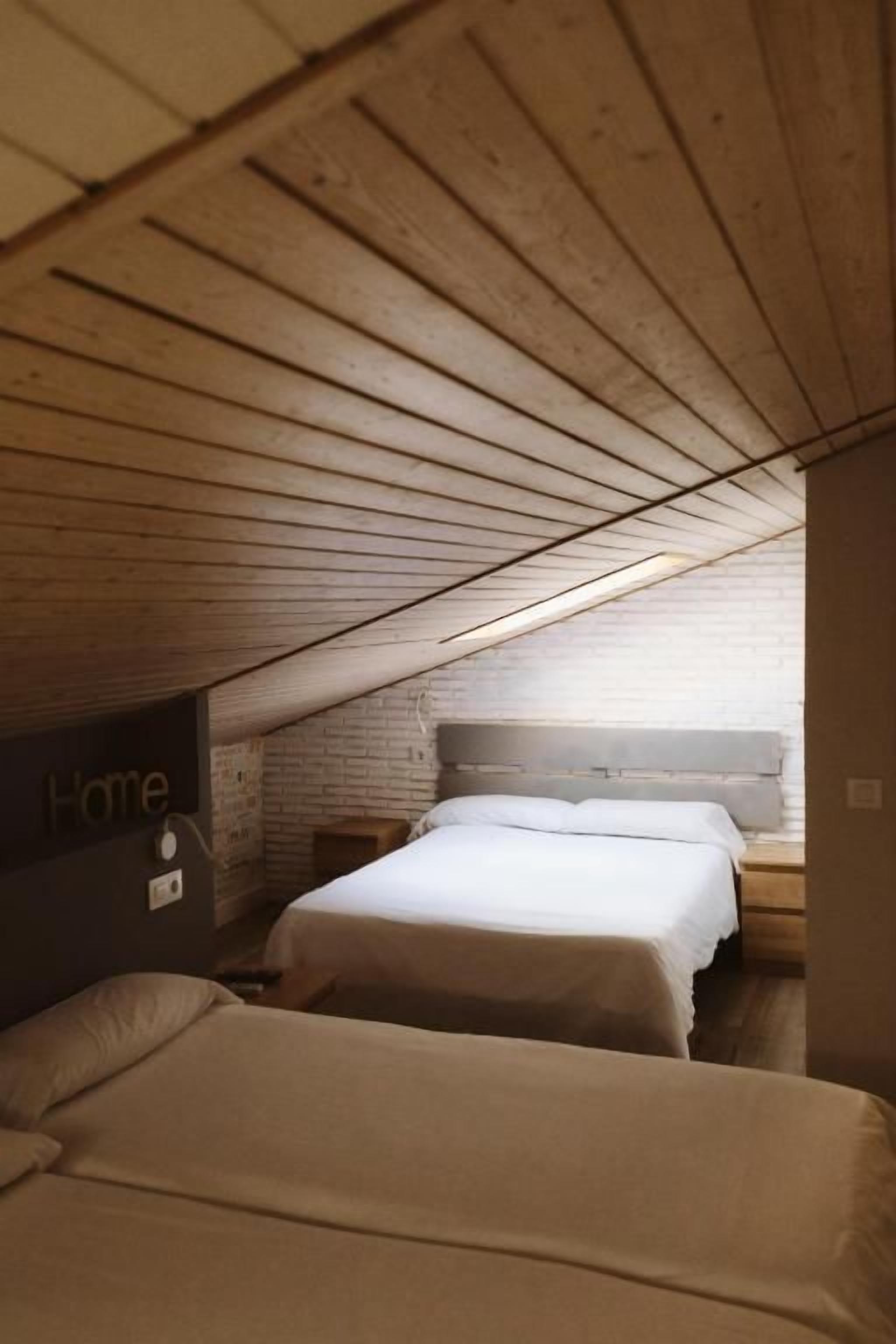 Una habitación con dos camas, techo de madera y pared de ladrillo.