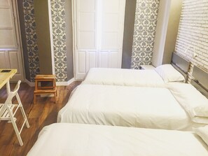 A room with two beds, a small wooden stool, a table, and patterned curtains. - Hostal Le vintage (Ávila)