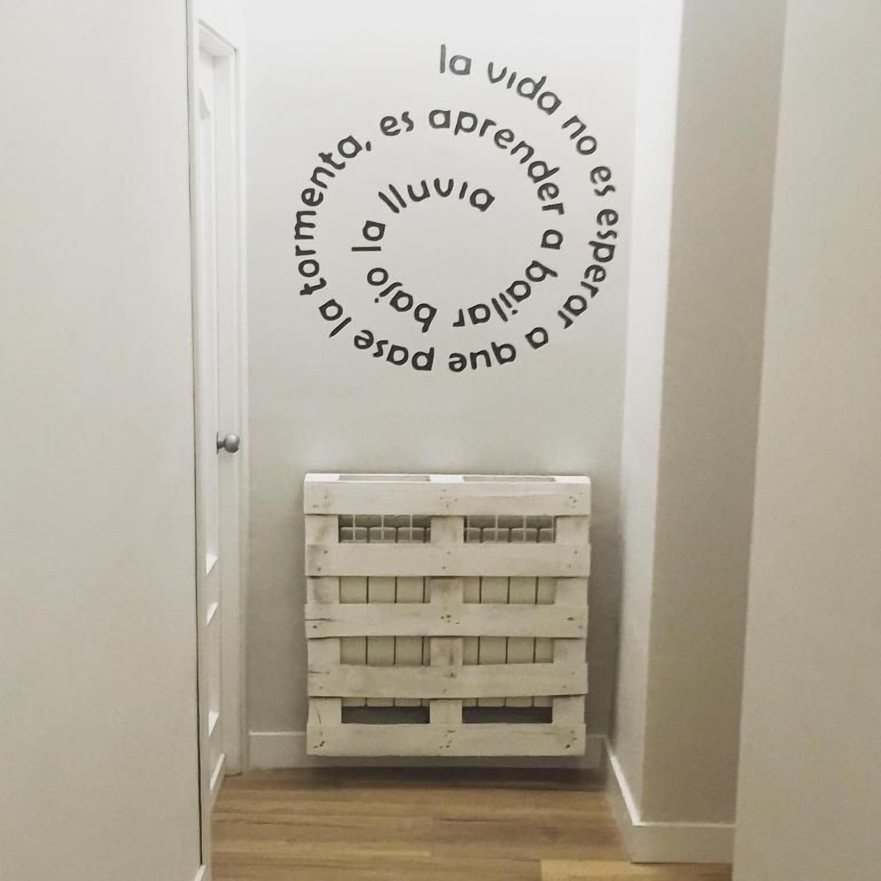 A hallway with a white door, a white wall with a circular text design, and a white crate.