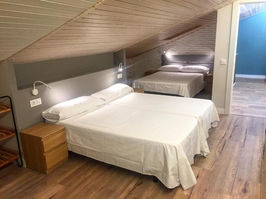 A room with two beds, a nightstand, and a wooden ceiling.