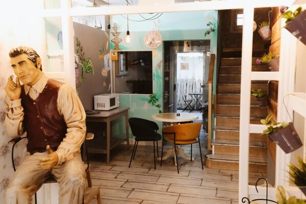 A room with a wooden floor, a table with chairs, a microwave, and a staircase with potted plants. - Hostal Le vintage (Ávila)