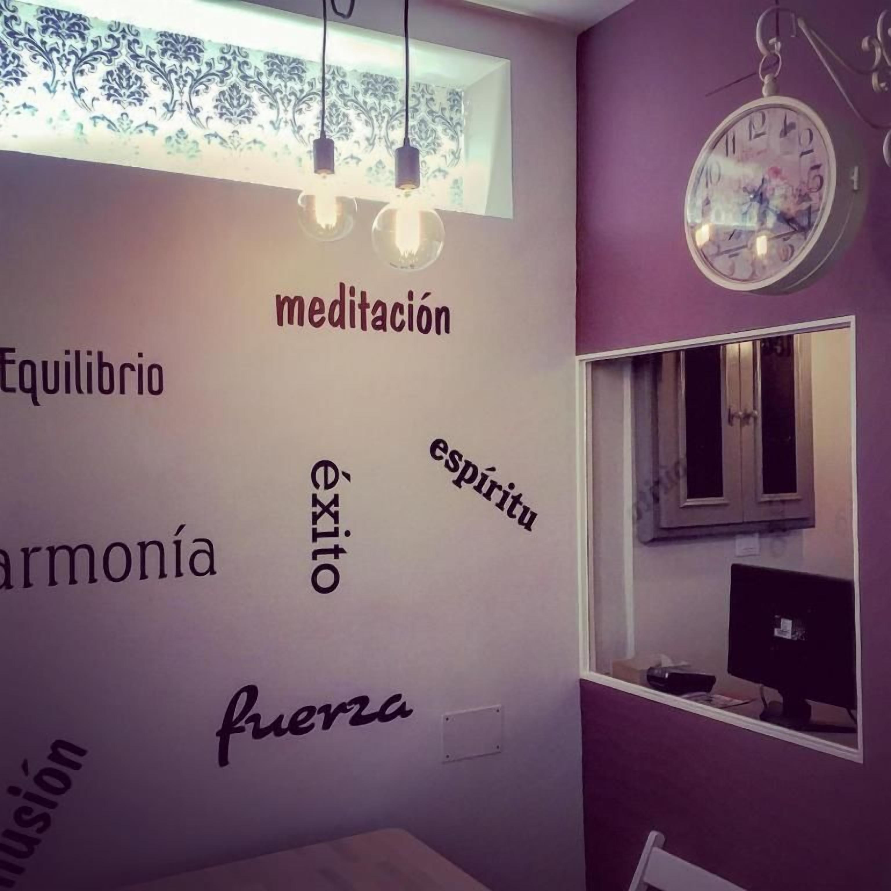A room with a wall decorated with words like 'equilibrio,' 'armonía,' 'éxito,' 'espíritu,' and 'fuerza.' There is a window with a computer monitor and a chair.