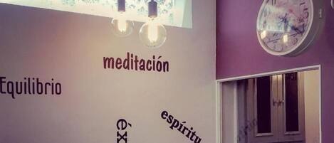 A room with a wall decorated with words like 'equilibrio,' 'armonía,' 'éxito,' 'espíritu,' and 'fuerza.' There is a window with a computer monitor and a chair.