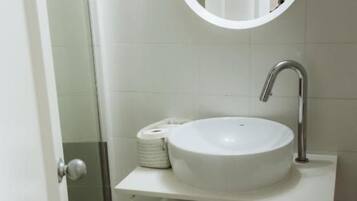 A bathroom with a white sink, a round mirror, and a towel dispenser.