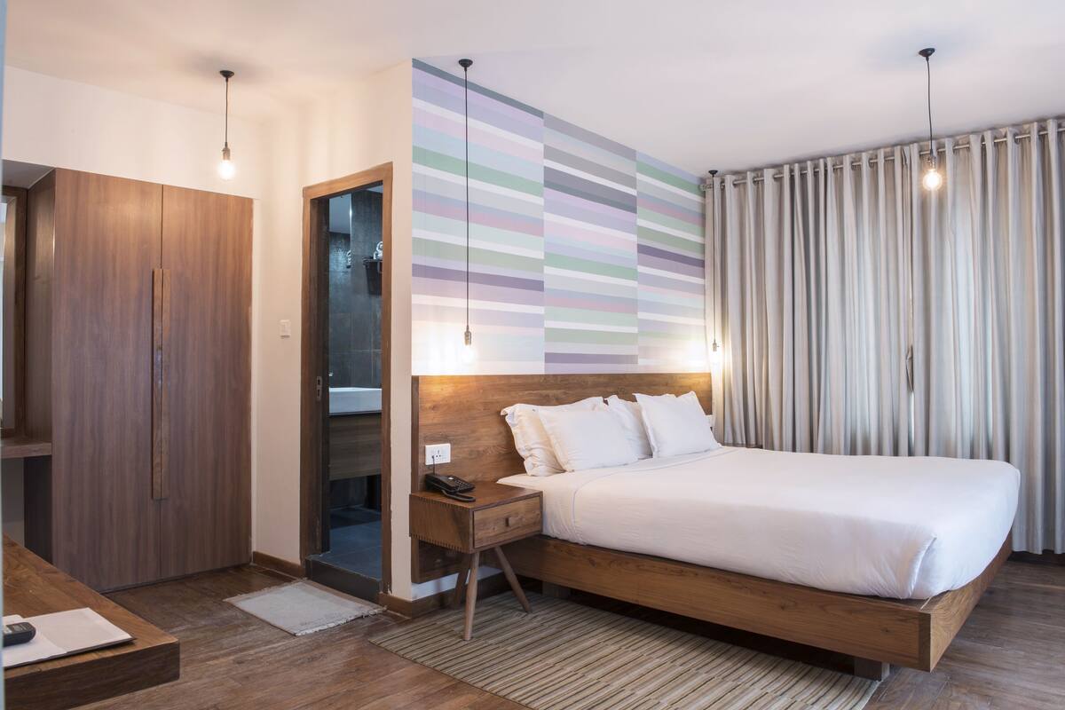 A modern hotel room with a wooden bed, a nightstand, a wardrobe, and a striped wall.