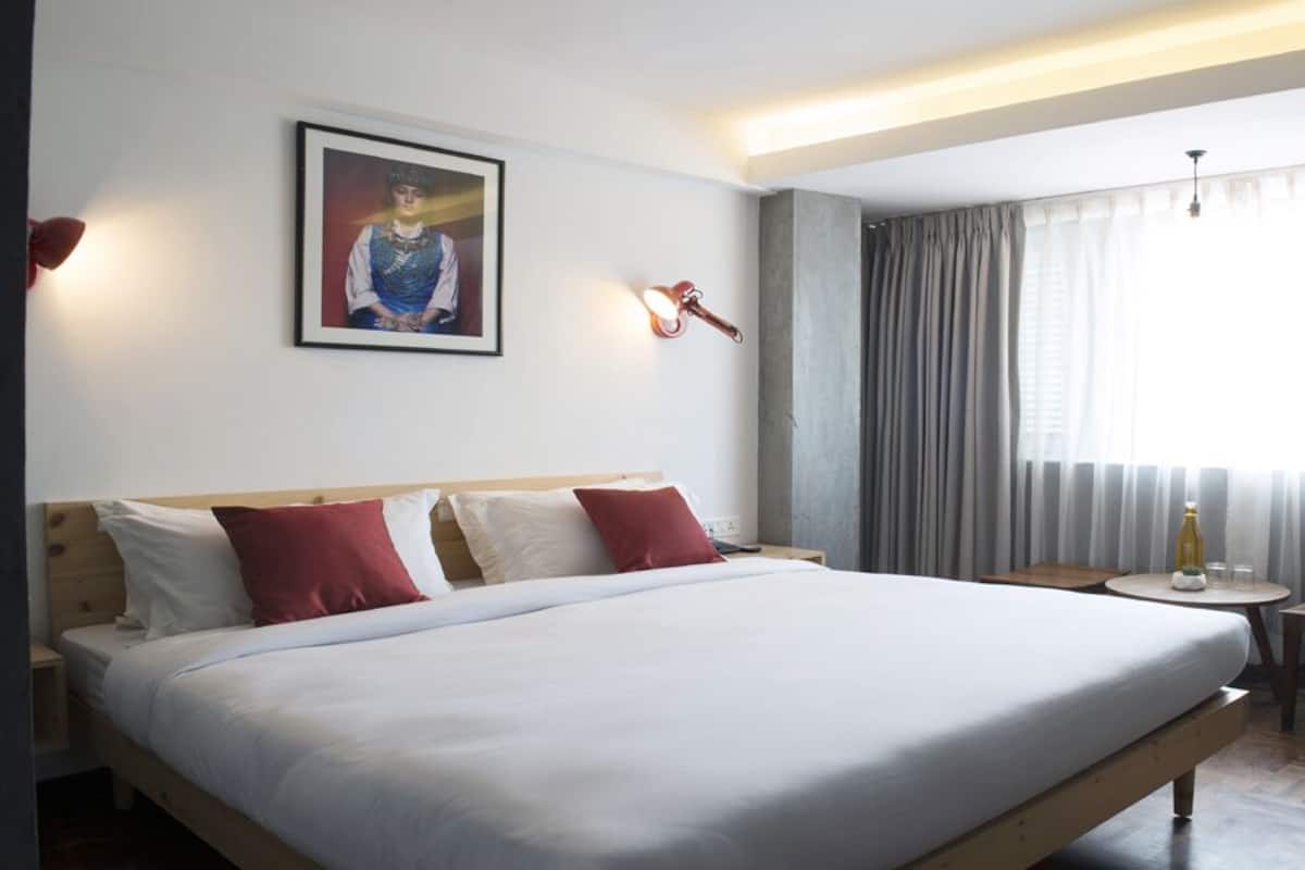A hotel room with a large bed, a bedside table, a small table, a lamp, and a window with curtains.
