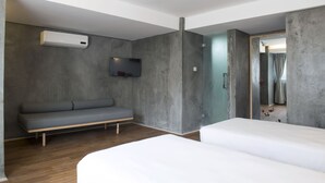 Una habitación de hotel moderna con un sofá gris, una cama y un televisor fijado en la pared.