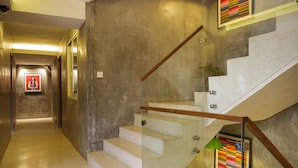 Un interior moderno con una escalera de cristal, un pasillo con un cuadro enmarcado y una planta en maceta sobre un mueble.