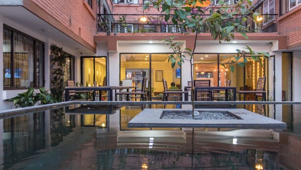 Un vestíbulo de hotel con piscina de cristal, plantas de interior y zonas de estar.