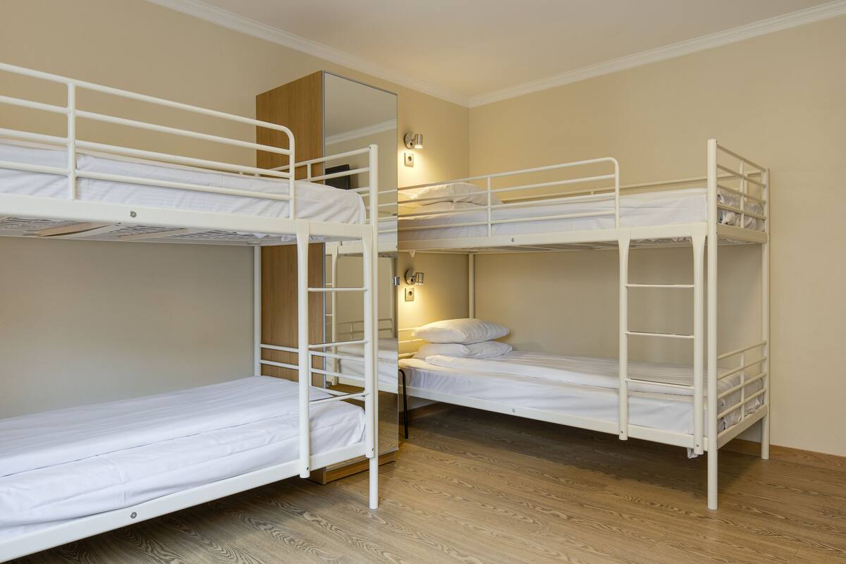 Una habitación con tres literas, suelo de madera y una lámpara fijada a la pared.