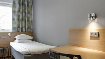 Habitación de hotel con cama, escritorio, silla, ventana con cortinas y un enchufe en la pared.