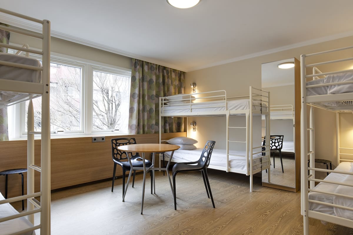 Habitación con literas, una mesa de madera y sillas, una ventana con cortinas y un espejo en la pared.