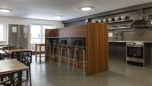 Una cocina moderna con electrodomésticos de acero inoxidable, taburetes de bar de madera y un área de estar con mesas y sillas.