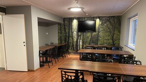 Un salón de conferencias con una gran mesa y sillas, un televisor de pantalla plana montado en la pared, y un mural de un bosque en la pared de fondo.