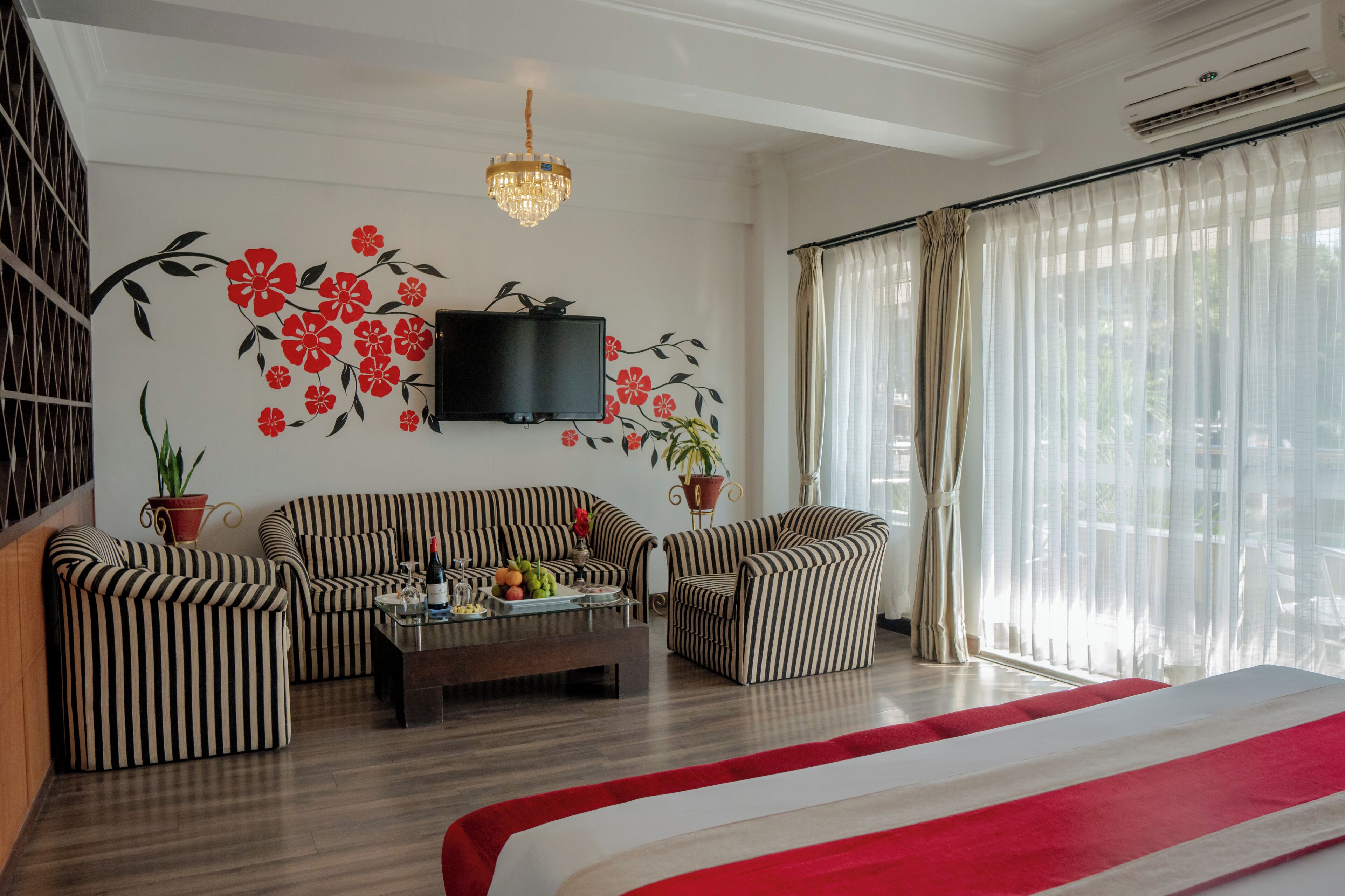 A living room with striped sofas, a coffee table with fruit, a TV, and a large window with curtains.