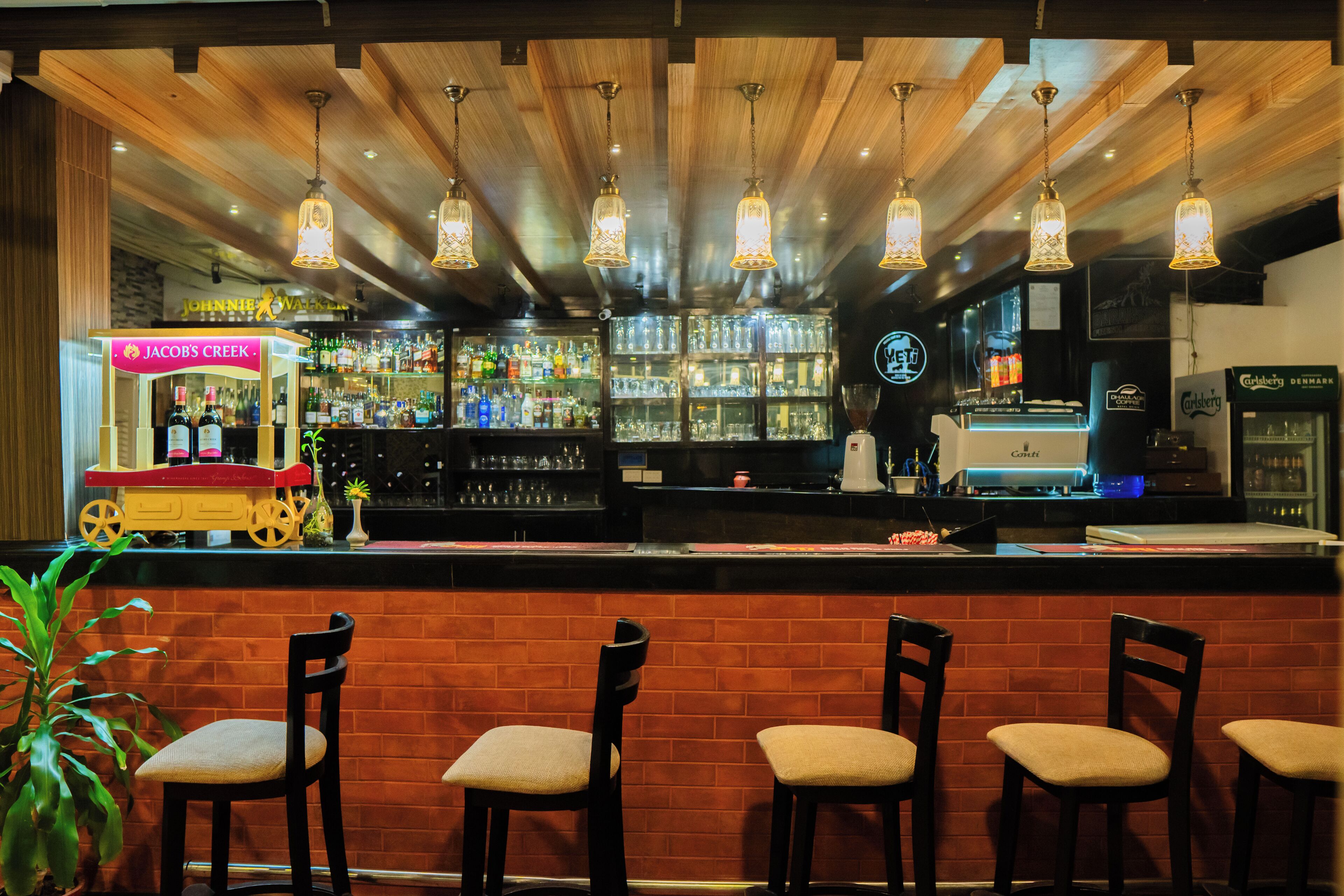 Een bar met houten plafond, hangende lampen en een toog met een displaykast.