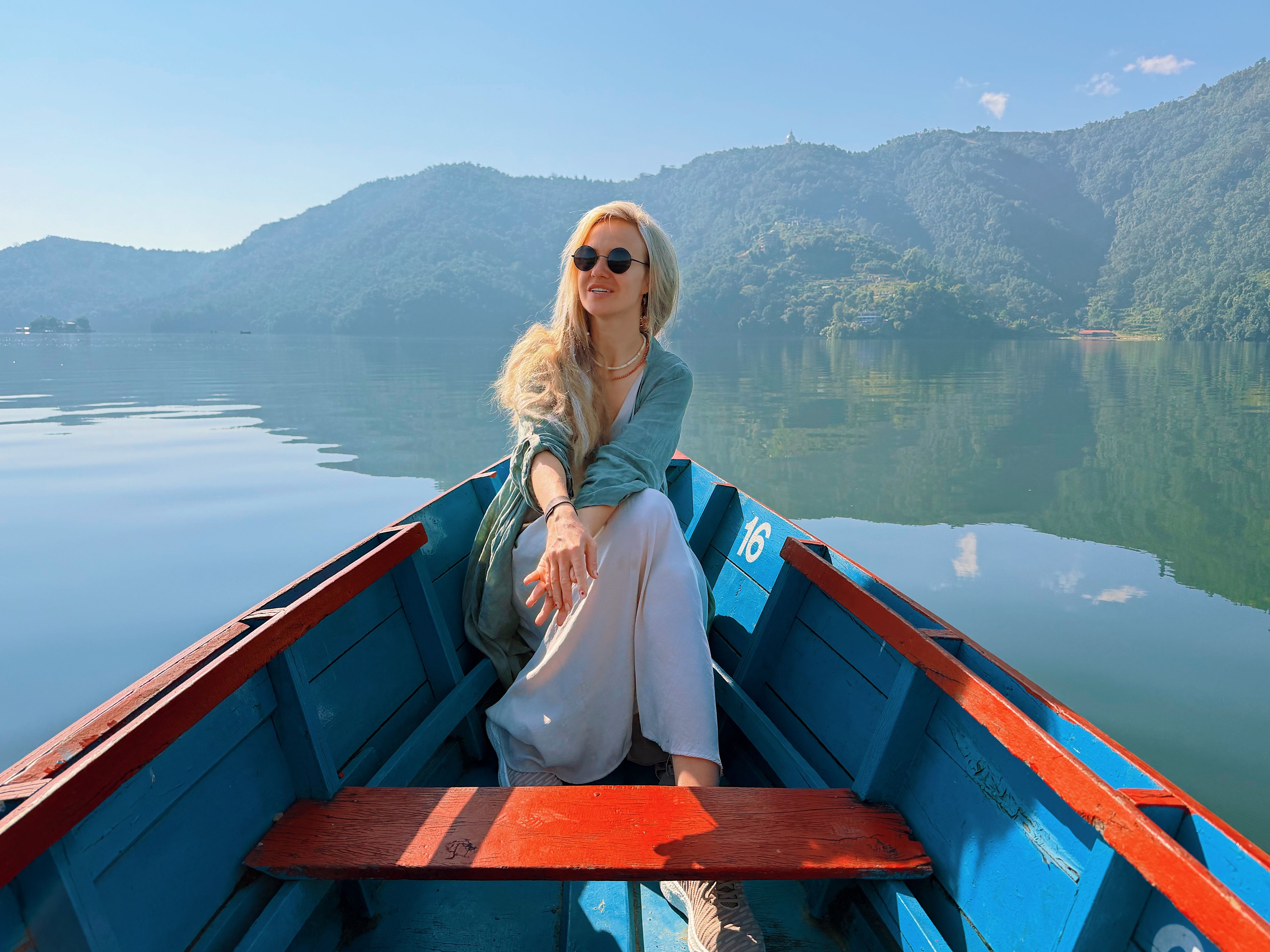 A person sitting in a boat with a view of calm water and mountains in the background.
