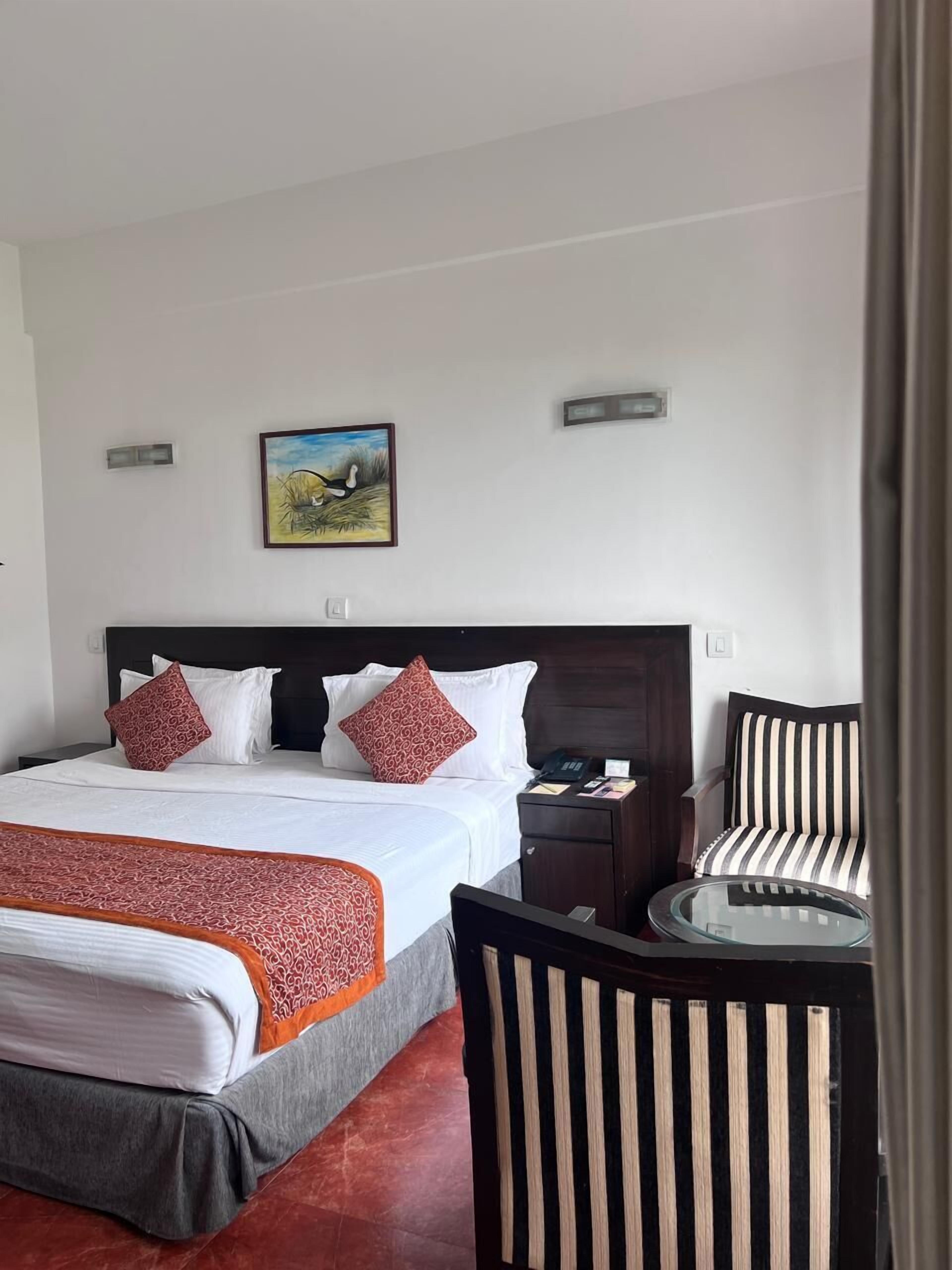 Une chambre d’hôtel avec un grand lit, deux oreillers, une table de chevet, une chaise, une petite table et un tableau au mur.