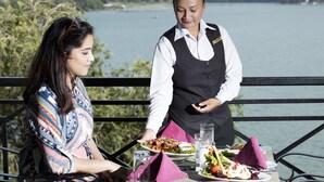 A dining table with plates of food, glasses, and a waiter serving a meal. - Waterfront Resort by KGH Group (Pokhara)