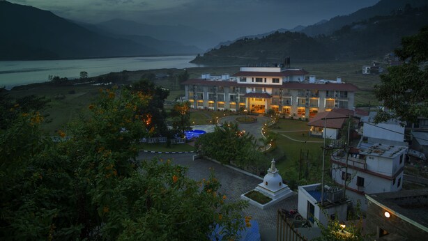 A large, multi-story building with a central courtyard, surrounded by lush greenery and overlooking a body of water. - Waterfront Resort by KGH Group (Pokhara)