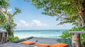A hammock with orange cushions on a wooden deck overlooking a beach with boats in the water. - Baan Ploy Sea (Rayong)