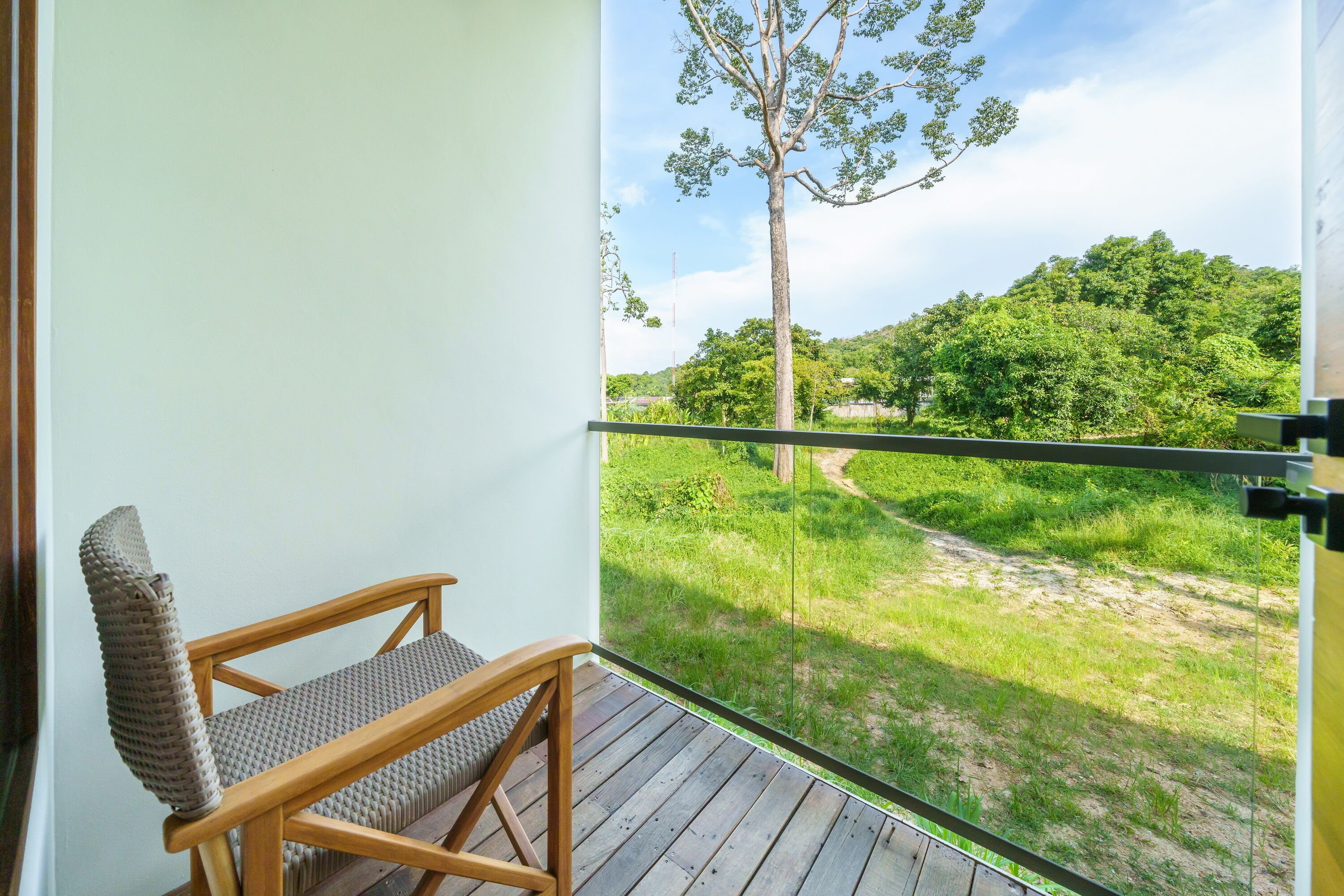 A balcony with a wooden chair and a view of a green landscape.