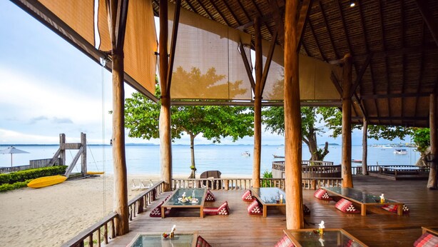 A beachside restaurant with wooden tables and red cushioned seating, overlooking the sea. - Baan Ploy Sea (Rayong)