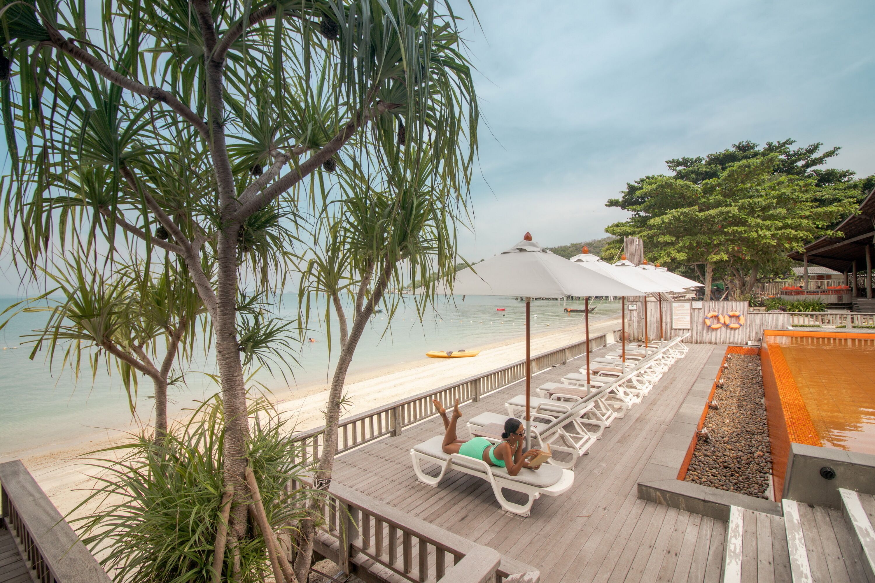 A wooden deck with lounge chairs and umbrellas overlooking a beach and pool area.