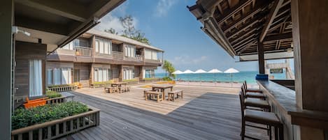 A wooden deck with outdoor seating, a bar area, and a view of the ocean.