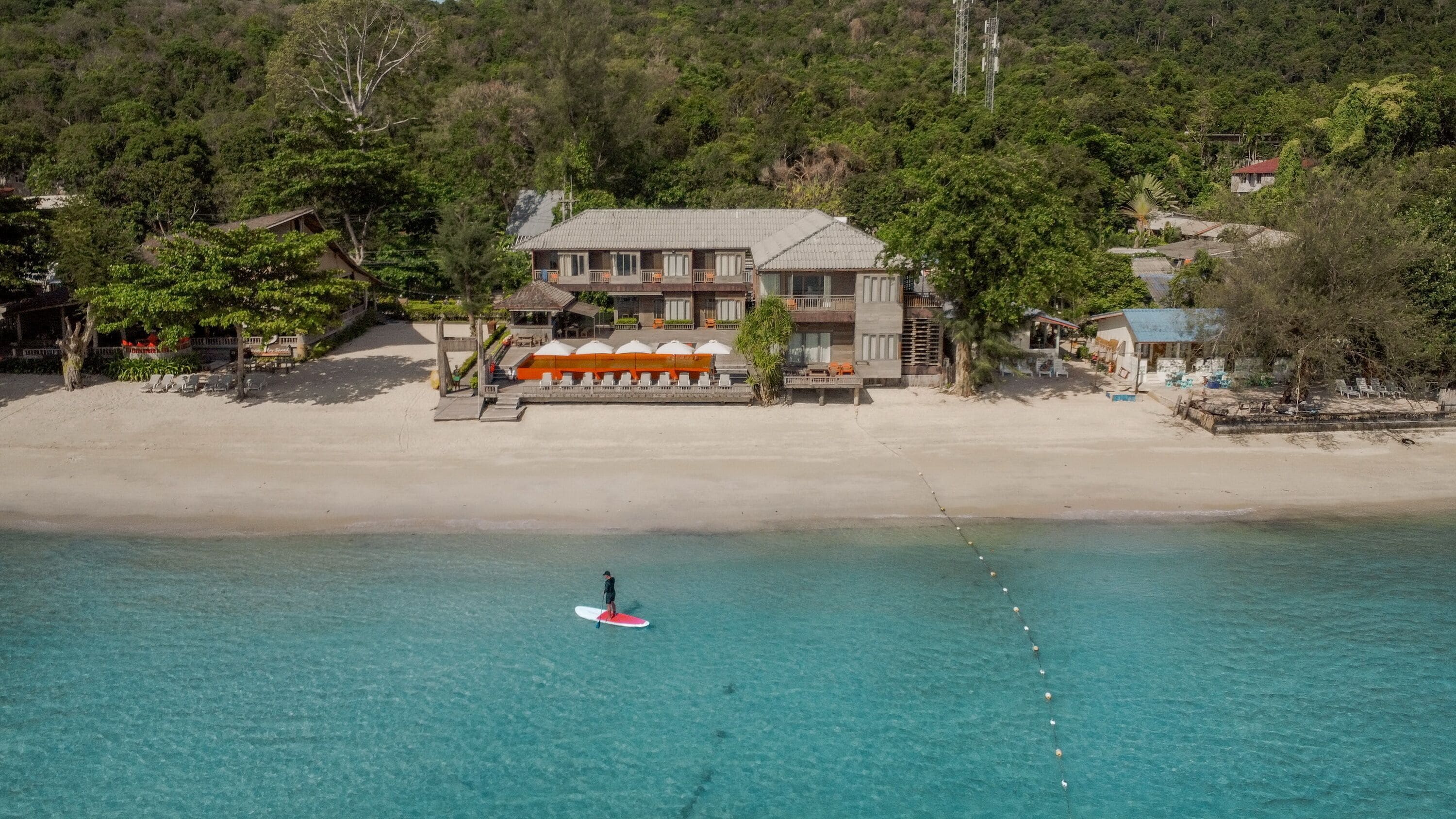 A beachfront property with a large building, a sandy beach, and a clear blue sea.