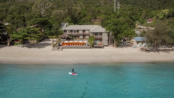 Una propiedad frente a la playa con un edificio grande, una playa de arena y un mar azul cristalino.