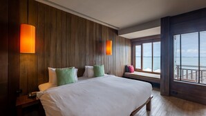 A hotel room with a large bed, wooden panel walls, two wall-mounted lamps, a bench by the window, and a view of the sea. - Baan Ploy Sea (Rayong)