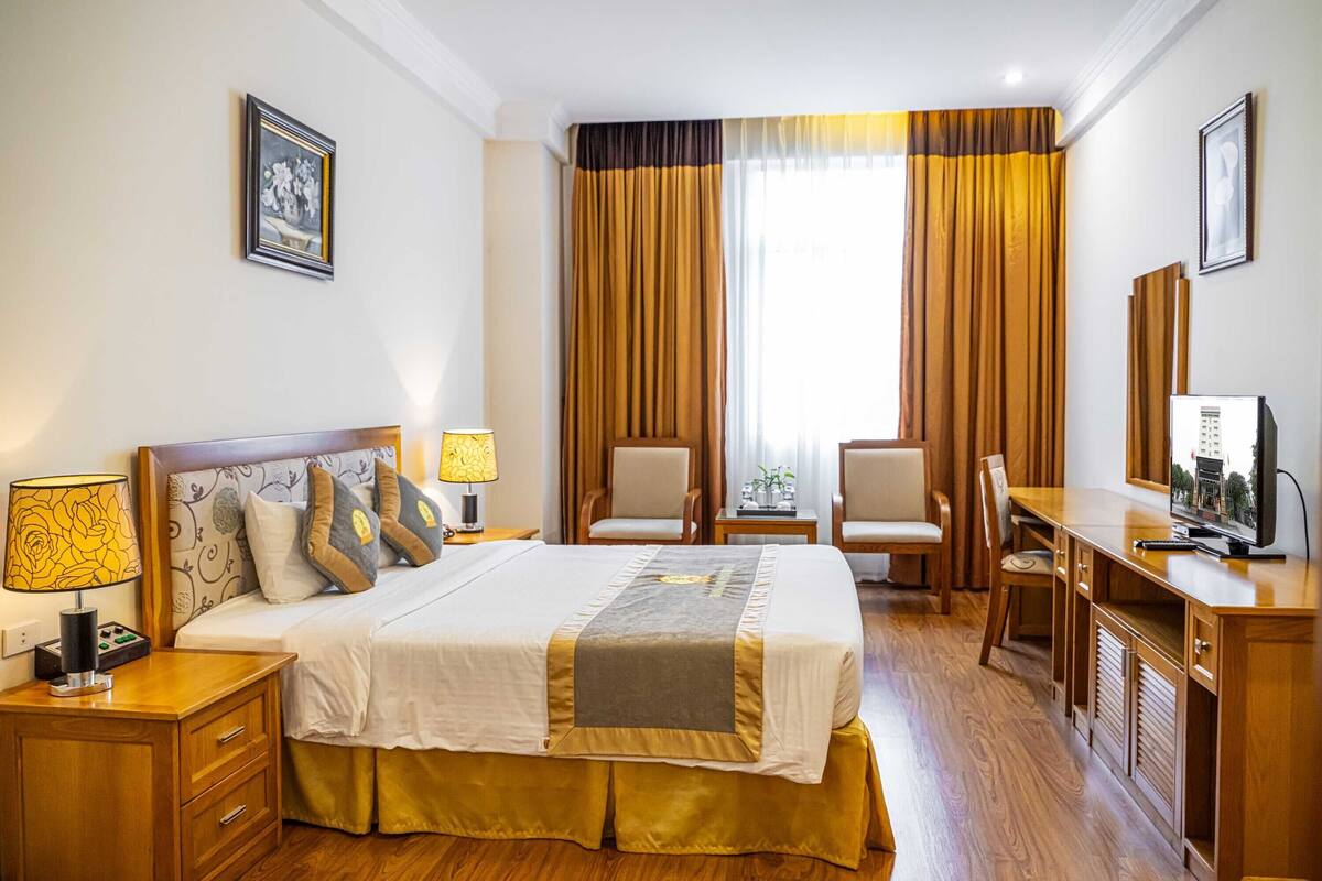 Ein Hotelzimmer mit einem großen Bett, zwei Sesseln, einem Schreibtisch und einem Fernseher.