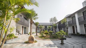 Une cour intérieure avec un jardin central, des allées pavées et des bâtiments dotés de balcons et de grandes fenêtres.
