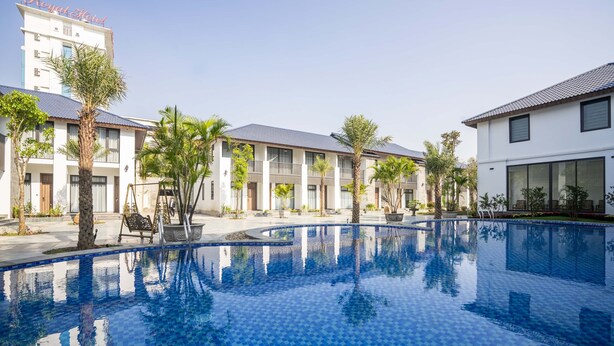 Un hôtel doté d’une piscine, de palmiers et d’un bâtiment surmonté d’un toit en tuiles.