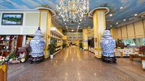 Un hall d’hôtel agrémenté d’un lustre, de deux grands vases et d’un comptoir d’accueil.