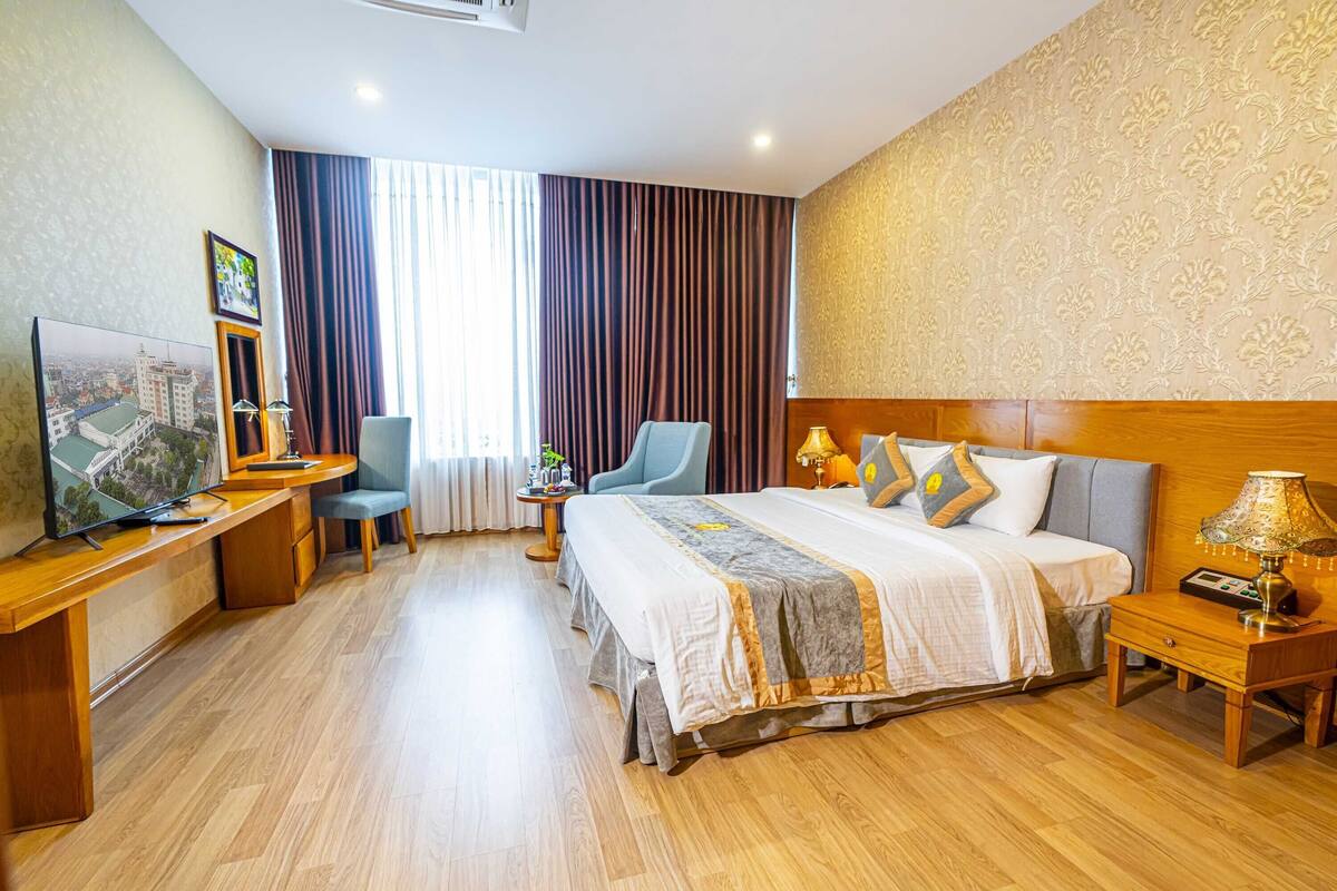 Ein Hotelzimmer mit einem großen Bett, einem Schreibtisch, einem Sessel, einem Fernseher und einem Nachttisch mit Lampe.