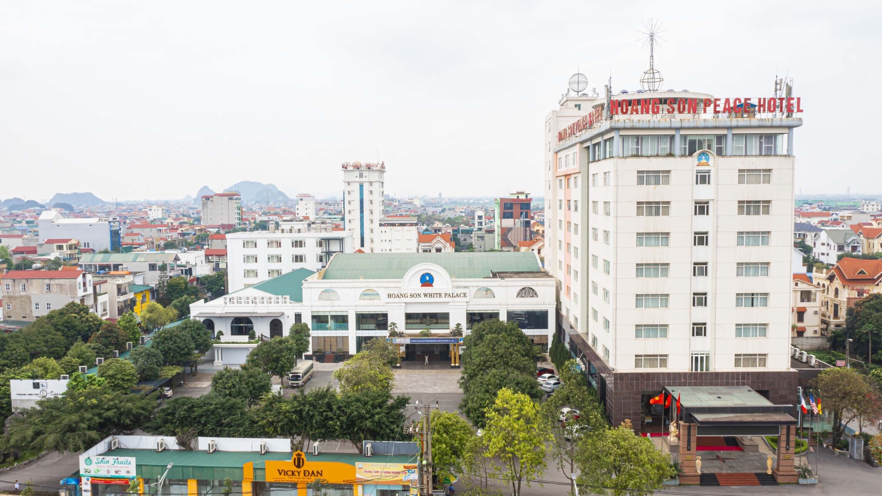 A hotel with multiple floors, a prominent sign, and a large building with a green roof labeled "HOANG SON WHITE PALACE".