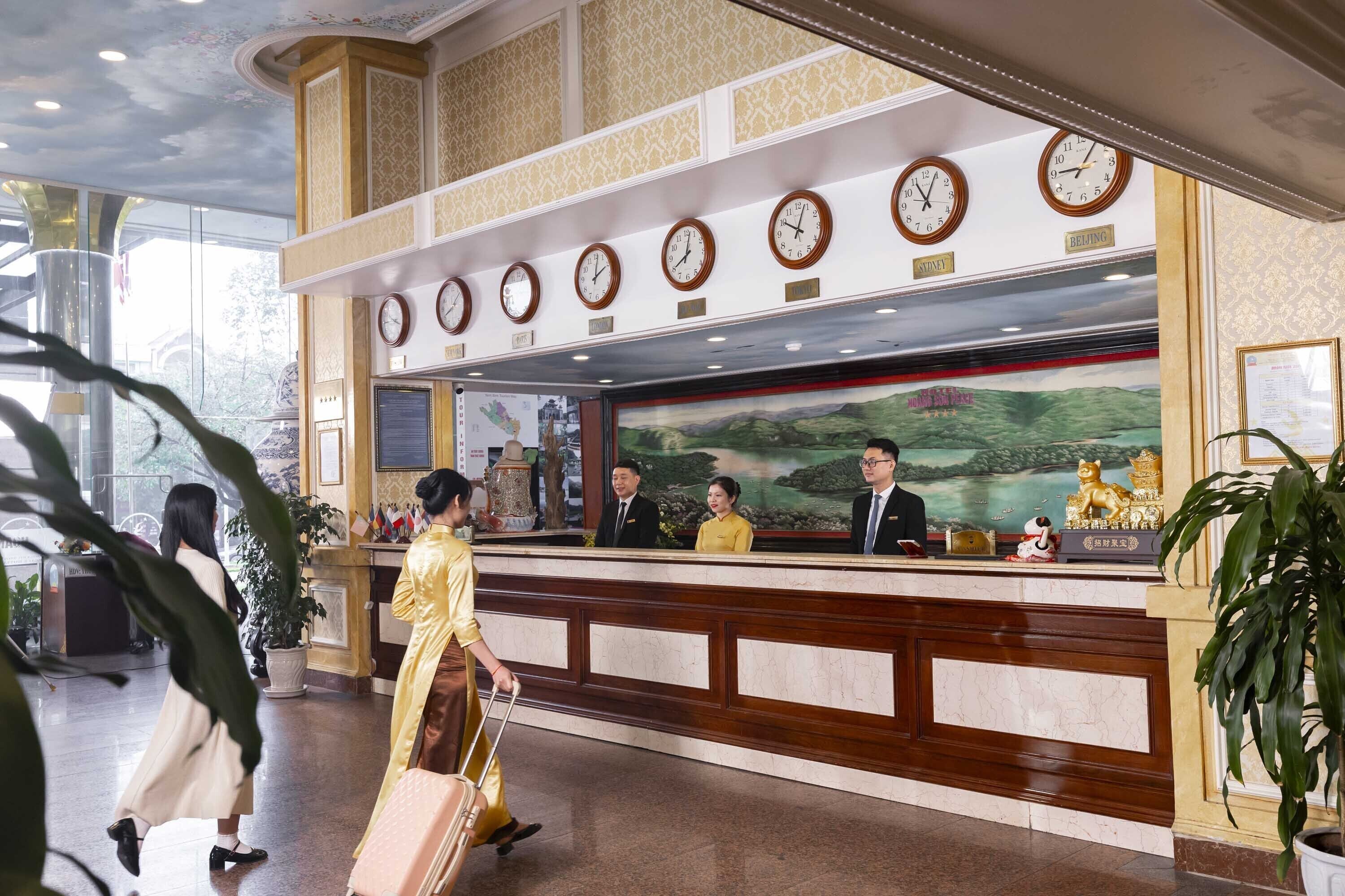 Zona de recepción de un hotel, con mostrador, varios relojes y un mural de un paisaje.