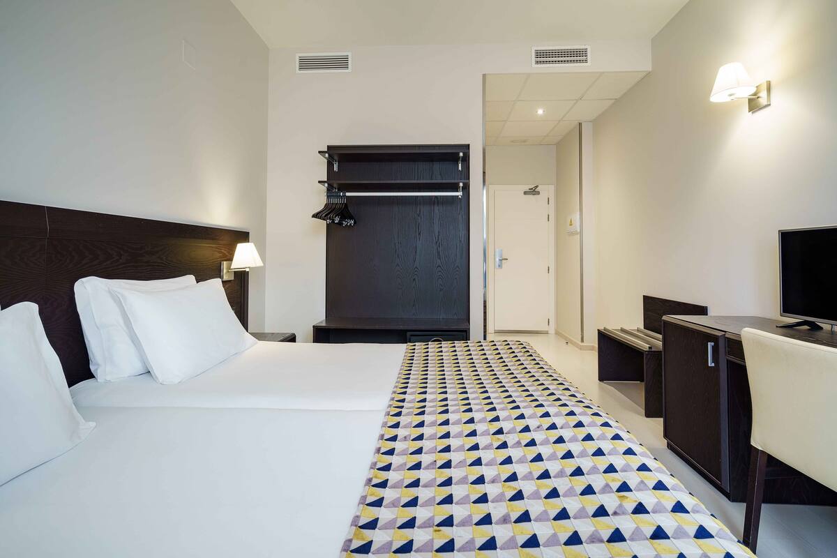 A hotel room with a bed, a desk, a TV, and a wardrobe.