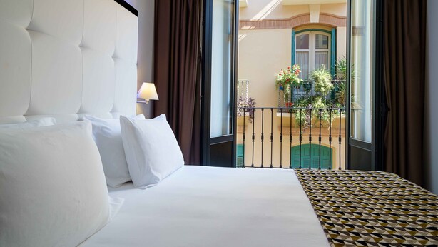 A hotel room with a large bed, a view of the outdoor balcony, and a window with curtains. - Dorma Málaga Museos (Málaga)