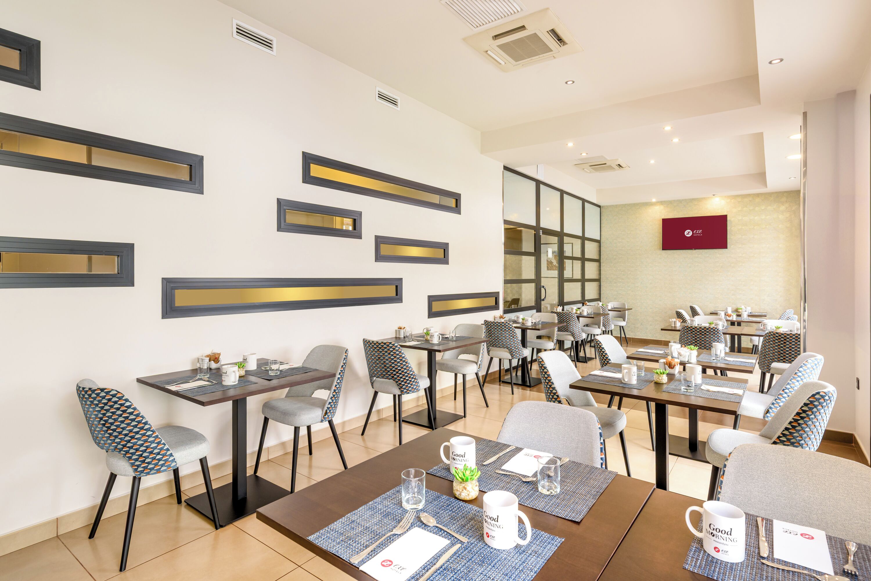 Een restaurantgedeelte van een hotel met meerdere tafels en stoelen, waarvan sommige zijn gedekt met tafelkleed en bestek.