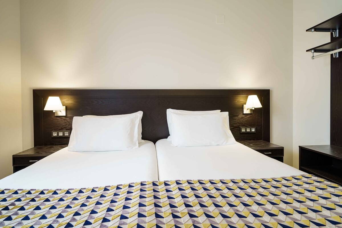 A double bed with a patterned bedspread, two bedside tables with lamps, and a dark wood headboard.