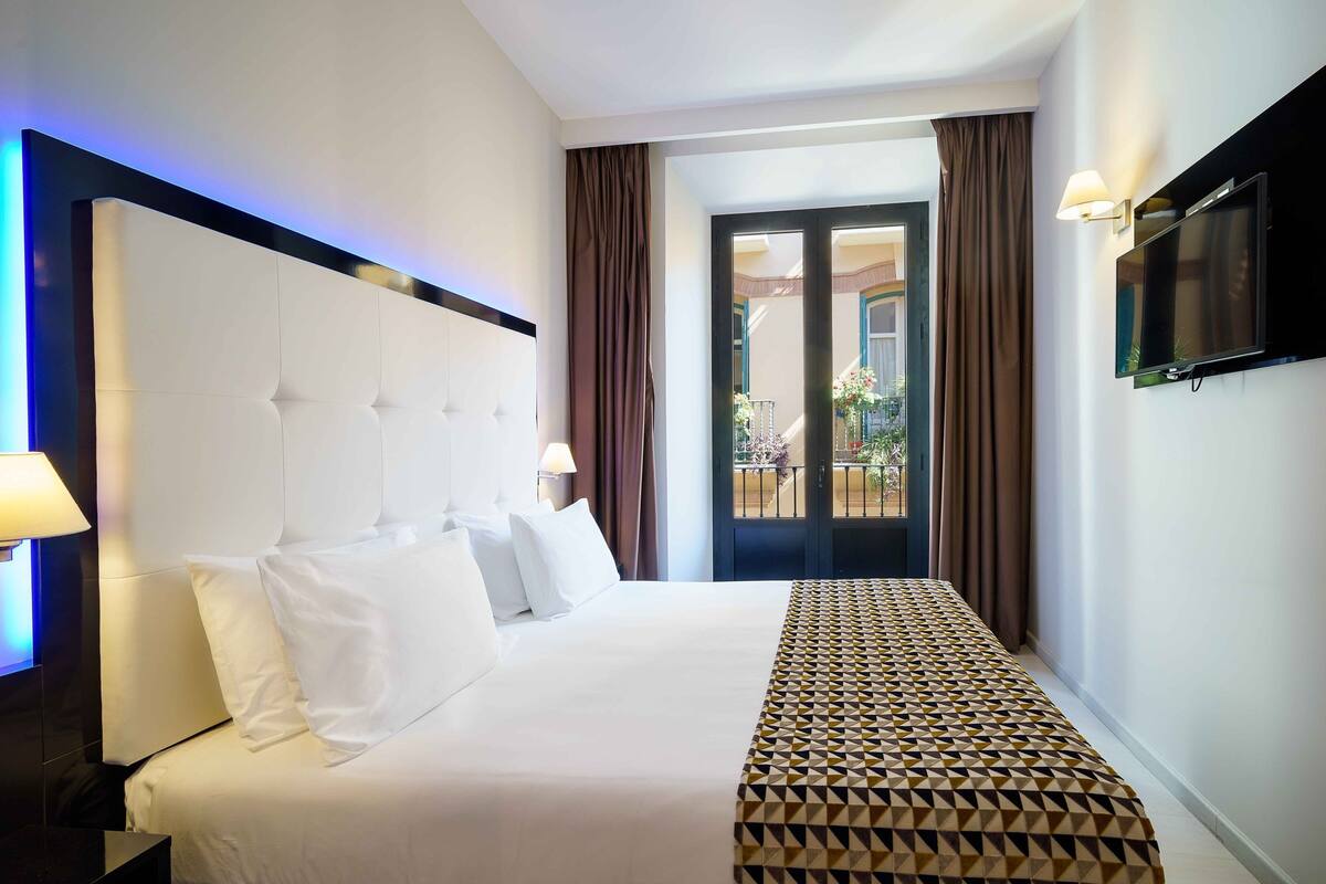 A hotel room with a large bed, a flat-screen TV, a nightstand, and a view of the outside balcony.