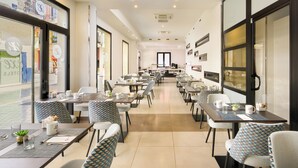 A spacious restaurant with multiple tables and chairs, a long counter, and large windows on one side. - Dorma Málaga Museos (Málaga)