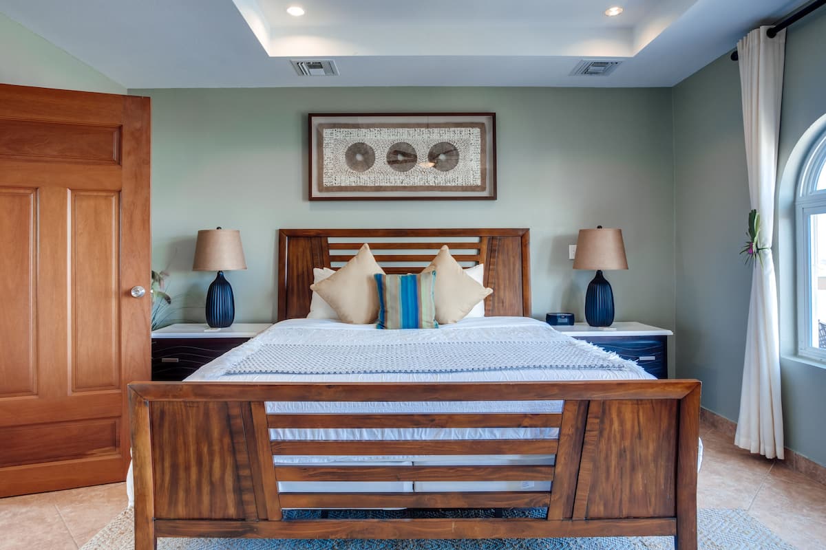 Un dormitorio con una cama de madera, dos mesitas de noche, un cuadro enmarcado sobre la cama y una ventana con cortinas.