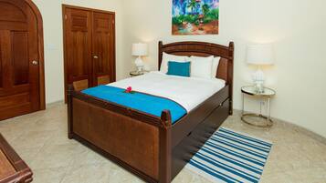 A hotel room with a wooden bed, a blue striped rug, and a painting of a tropical scene.