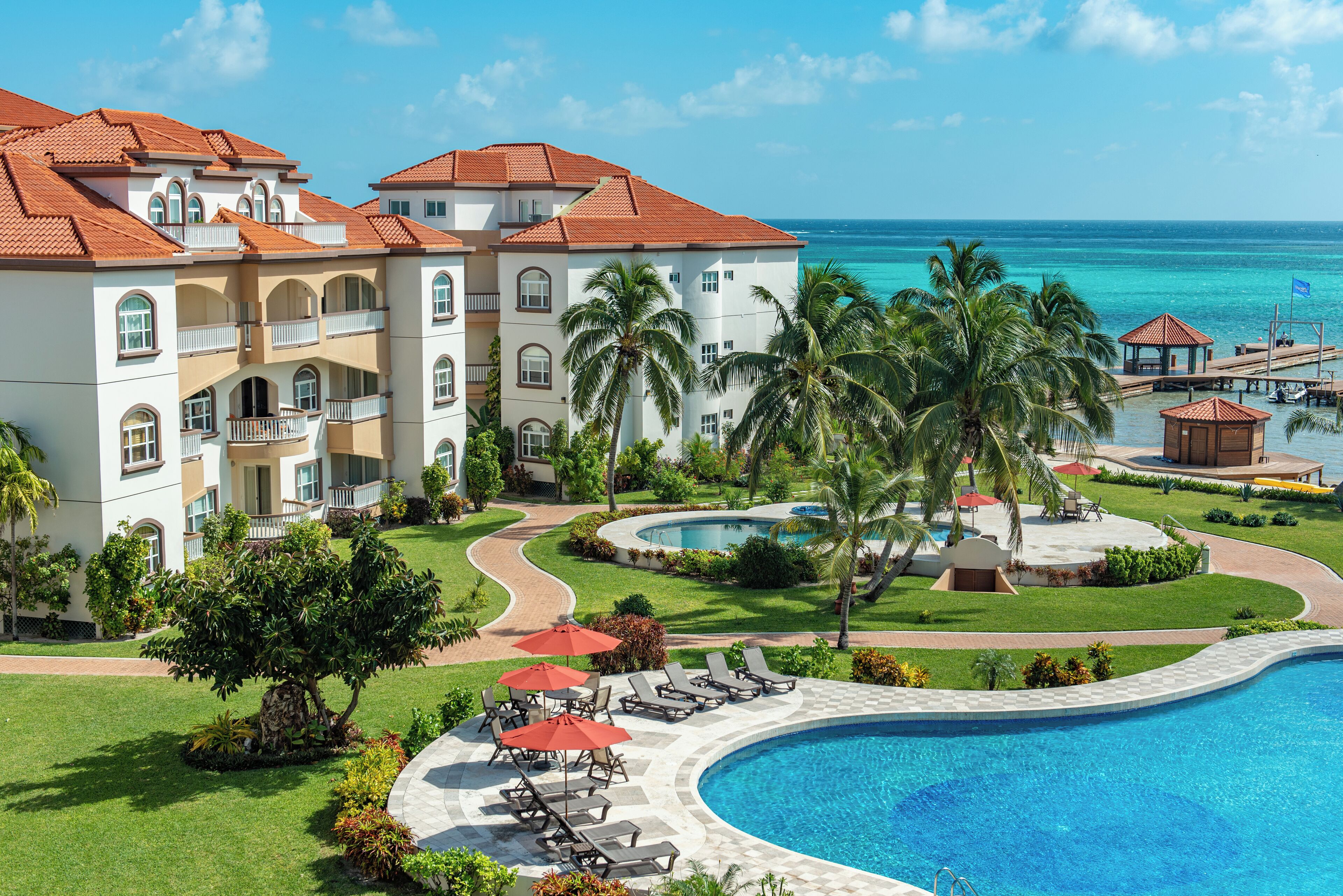Un resort con piscina, palmeras y vista al océano.