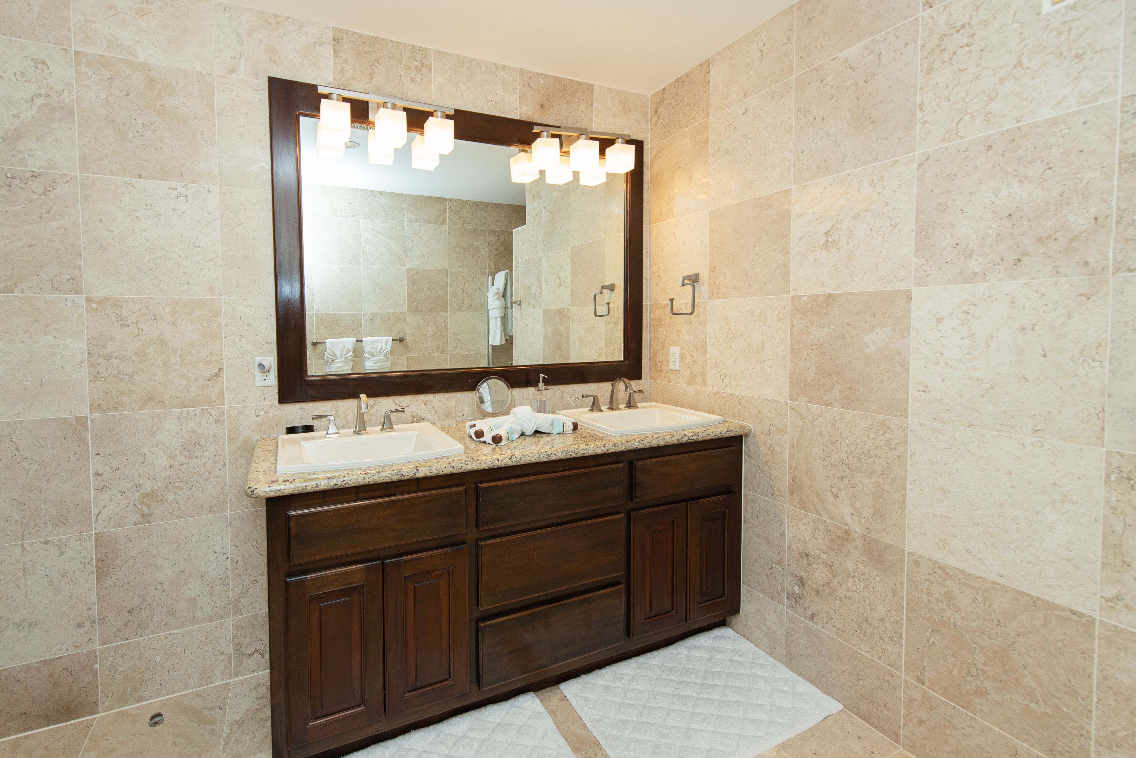 Un baño con un espejo grande, dos lavamanos y un mueble de tocador de madera oscura.